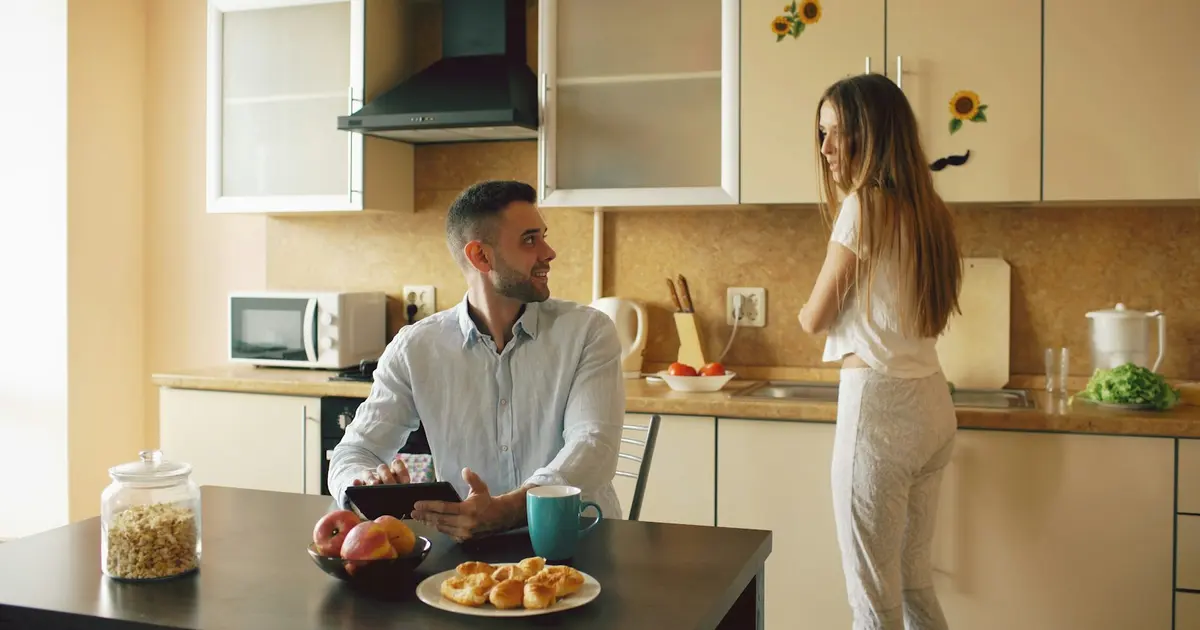 A couple talking across a kitchen table over breakfast