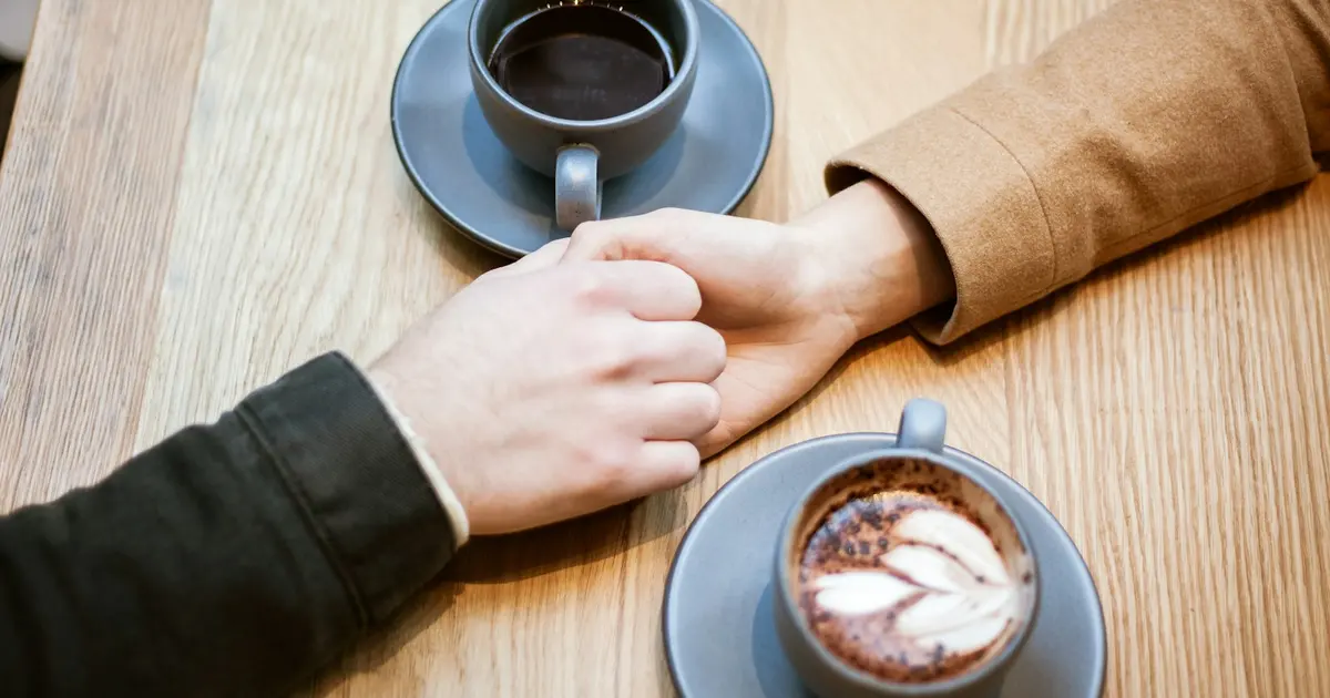 Two people holding hands between two cups of coffee on a table