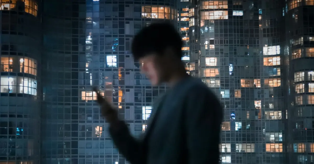 A man standing at a window, looking at his phone