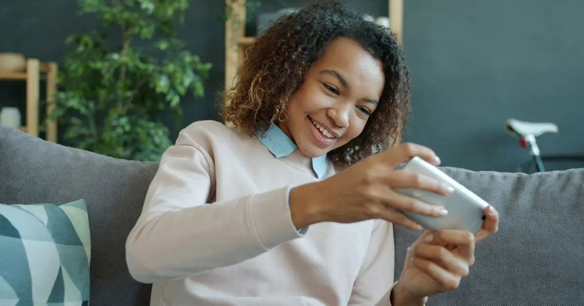 A young woman smiling at her phone on a sofa